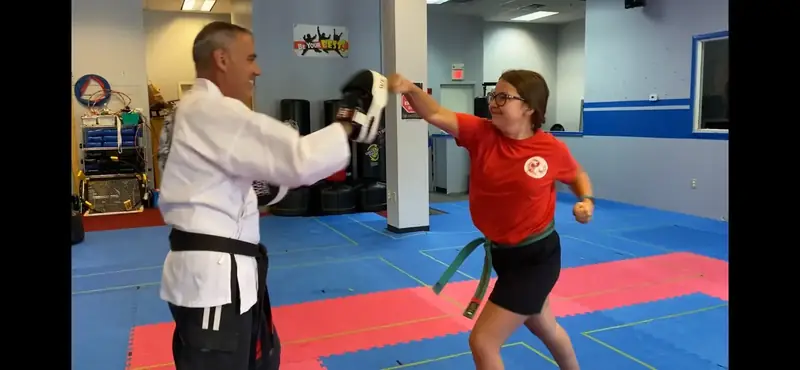 Teen student punching a focus mitt held by an instructor in a white gi in Hudson NH